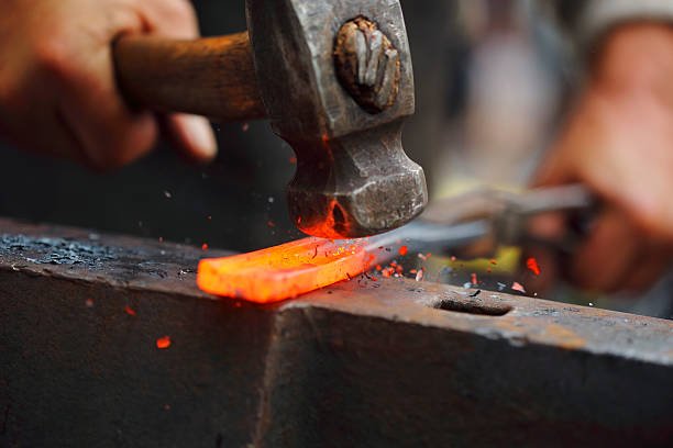 Detail shot of hammer forging hot iron at anvil